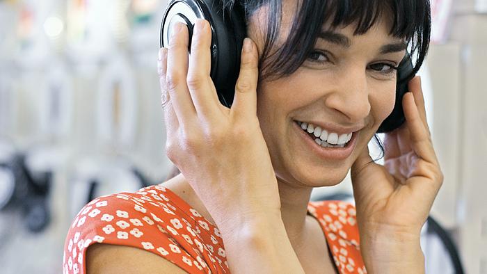 A woman an orange flower dress smiling about what she is hearing via her headphones