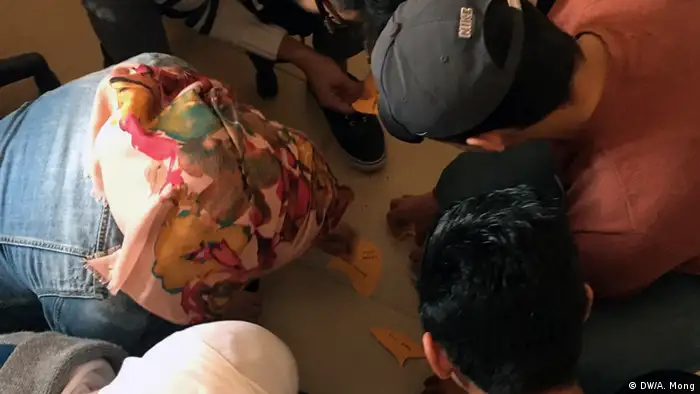 Five young people sit on the floor in order to write words on cards.