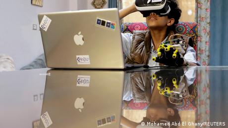 A teenager is seen wearing virtual reality devices on his eyes and left hand as he works from home