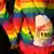 Duas pessoas de costas e de mãos dadas, vestidas com casacos nas cores do arco-íris, participam da marcha anual do orgulho LGBTQ do Christopher Street Day (CSD), em Berlim, Alemanha, em 23 de julho de 2022. Uma delas carrega uma bolsa onde se pode ler a palavra "Pride" ("orgulho" em inglês) num fundo colorido. 