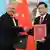 洪都拉斯外交部长雷纳（左）和中国外交部长秦刚3月26日在北京钓鱼台国宾馆举行的两国建交仪式上握手并秀出两国建交联合公报。