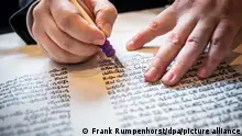 Hands of a person writing scriptures in Hebrew.