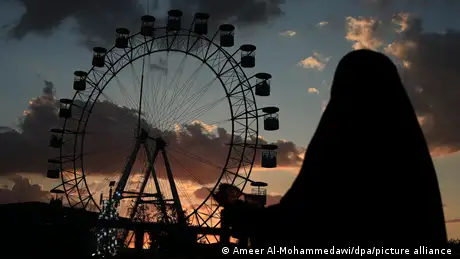 A woman watches a ferris wheel in an amusement park in Baghdad, Iraq.