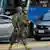 Dois militares armados andando; atrás deles há uma rua congestionada
